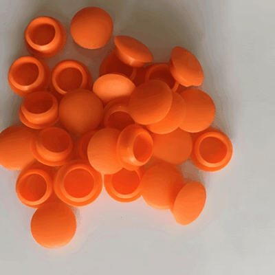 Pile of bright orange silicone end caps or rubber plug covers used for sealing tubes, fittings, or pipe ends