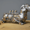 Steampunk dachshund dog sculpture with gears and pipes, silver resin finish, warm bulb background on wooden surface